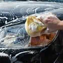 Hand washing a car with a sponge full of soap suds