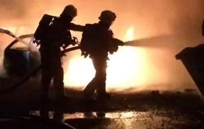 Silhouette of two firefighters in front of flames using a hose reel to extinguish a fire in an incident that destroyed 14 cars in a blaze in Langley