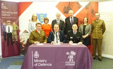 The chairman and other officials sat and stood around a table after signing the Armed Forces Covenant in front of the RBFRS banner