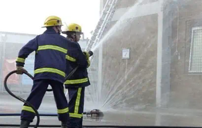 Two young firefighters using hose reels on a building