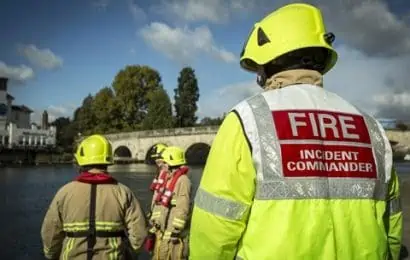 Three firefighters and one incident commander facing away from the camera looking onto water