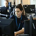Member of control staff sat working at her computer wearing a headphone set with microphone