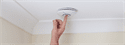 close up of finger pressing button on smoke alarm on ceiling