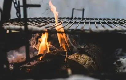 BBQ grill above flaming wood and logs