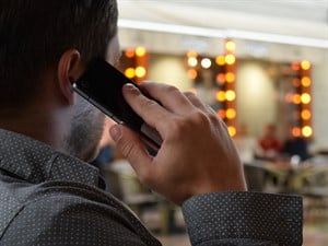 Man facing away with phone to his ear banner with cafe lights in the background