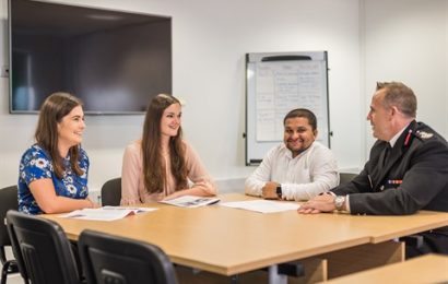 Photo banner of three Change 100 interns sitting around a table with chief fire officer Trevor Ferguson