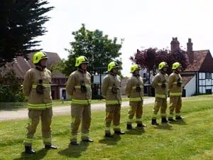 Six newly recruited firefighters standing in a row wearing uniforms and hats