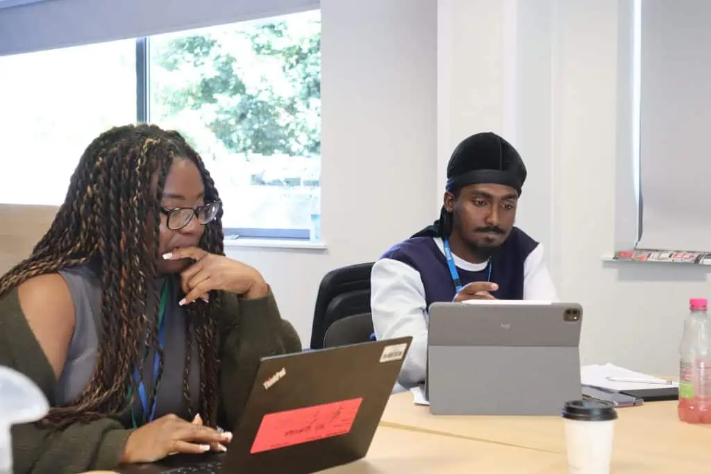 Two people sat next to eachother working on laptops.