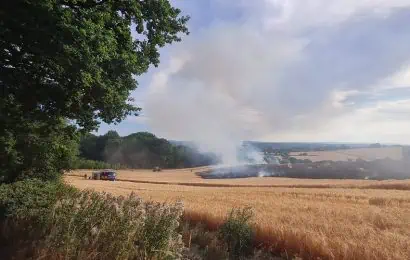 A fire in the open in a field with two fire appliances driving