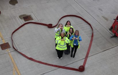 Five people posing in a heart made of hose reels