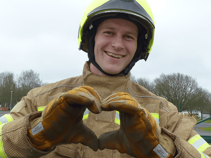 Firefighter in protective gear making a heart shape with hands outdoors, Royal Berkshire Fire and Re.