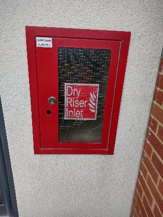 Red fire safety equipment cabinet with "Dry Riser Inlet" label.