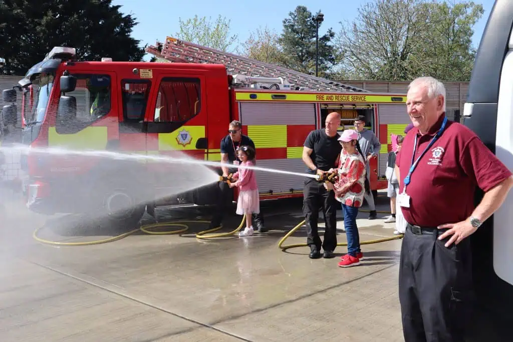 Two firefighters showing children how to use hose reels with a volunteer watching on in the foreground.