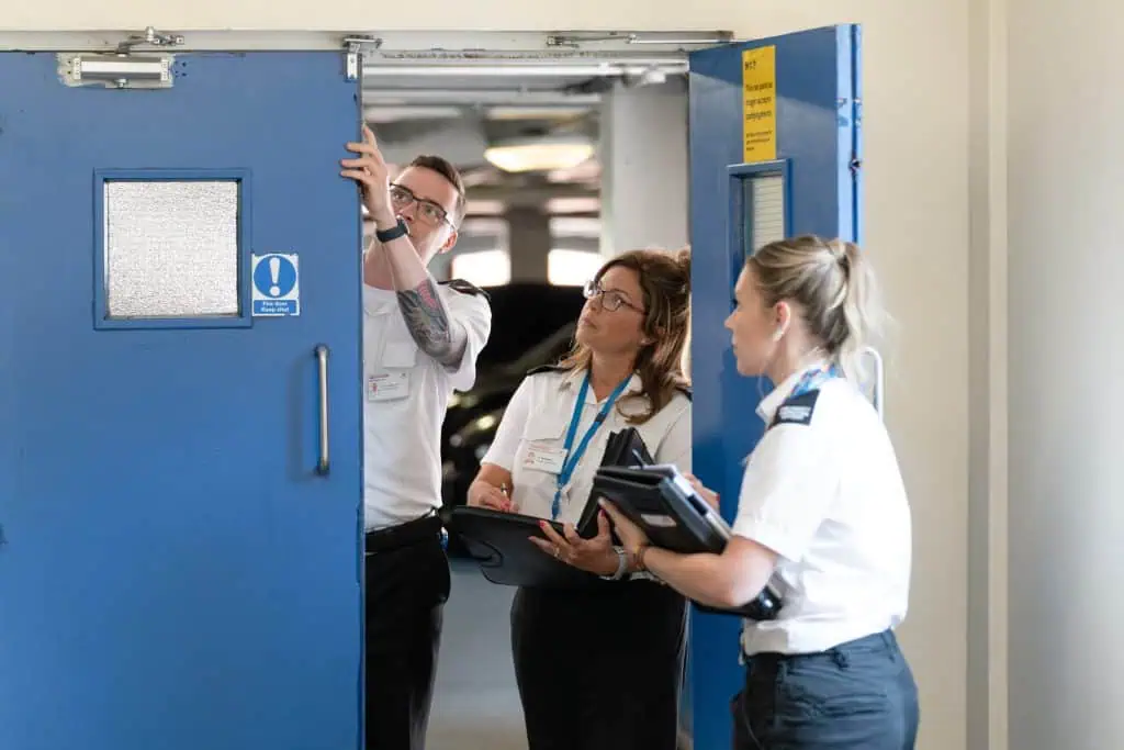 Three fire safety inspecting officers looking at a blue fire door.