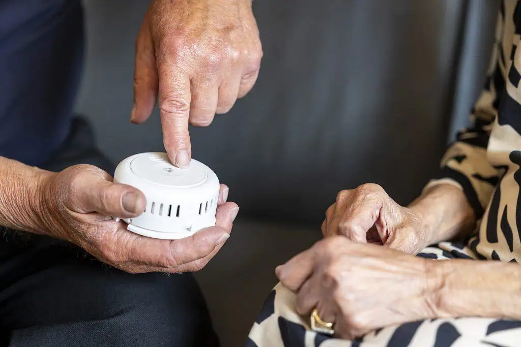 Pictured is an elderly couple testing a smoke alarm.