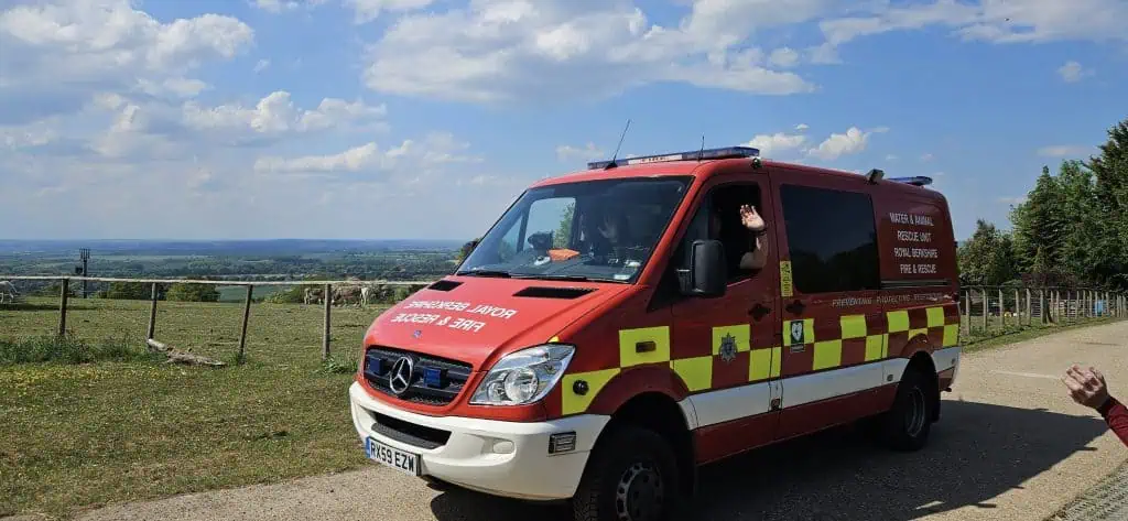 A red van with fire service branding driving down a country lane