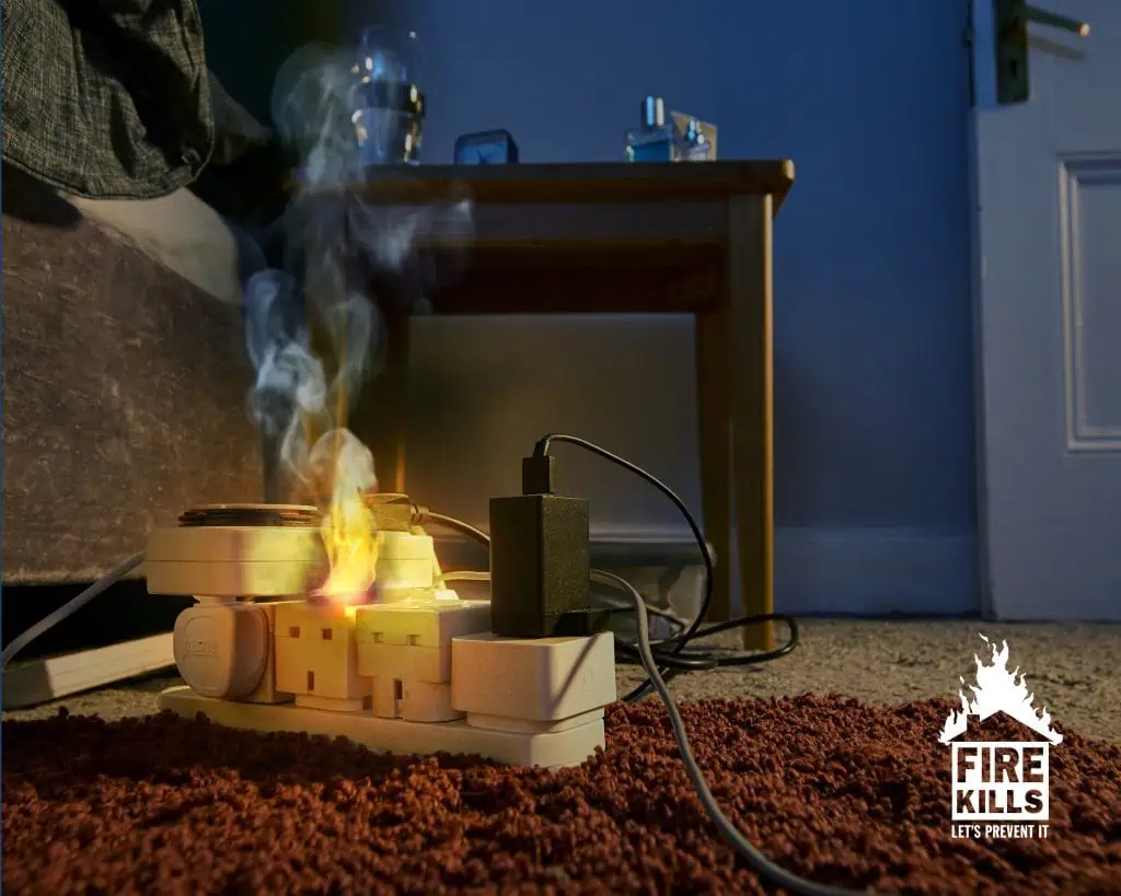 An extension cable overloaded with plugs. The plugs are on fire and producing smoke.