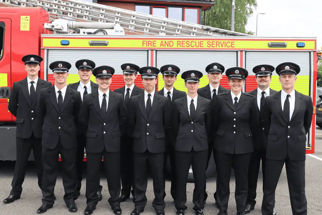 Twelve firefighters in undress uniform stood in front of a fire engine.