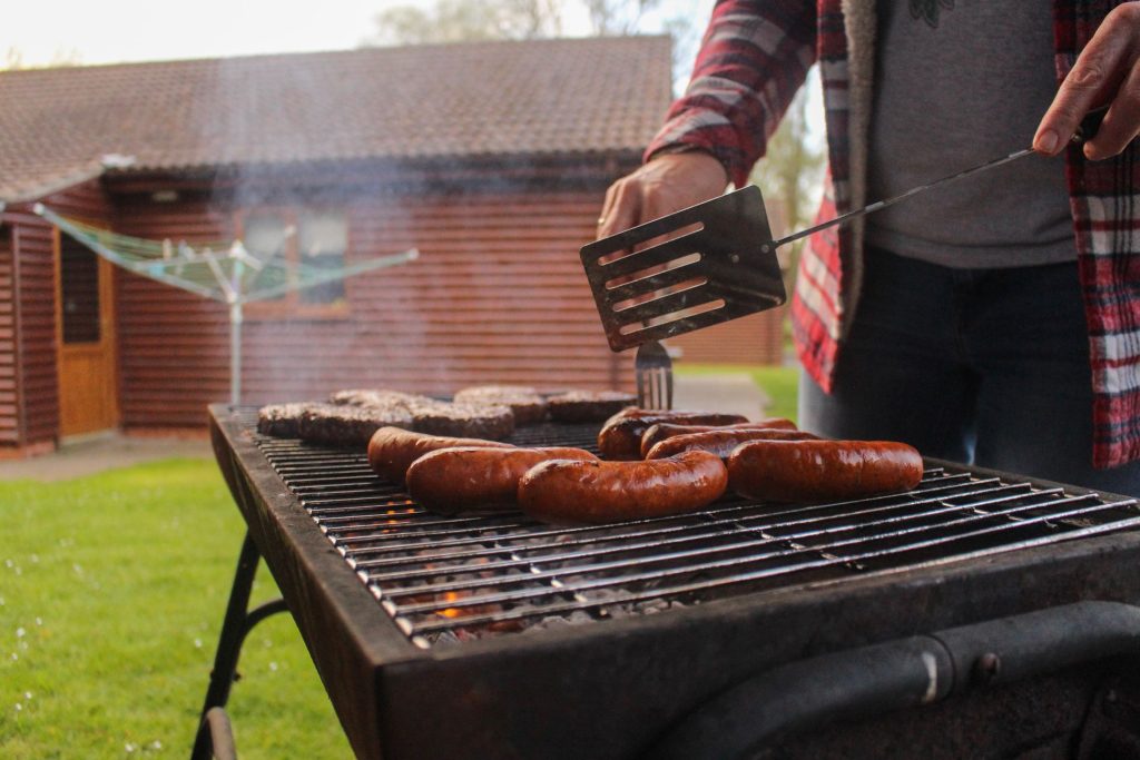 Person grilling sausages outdoors with fire safety awareness.